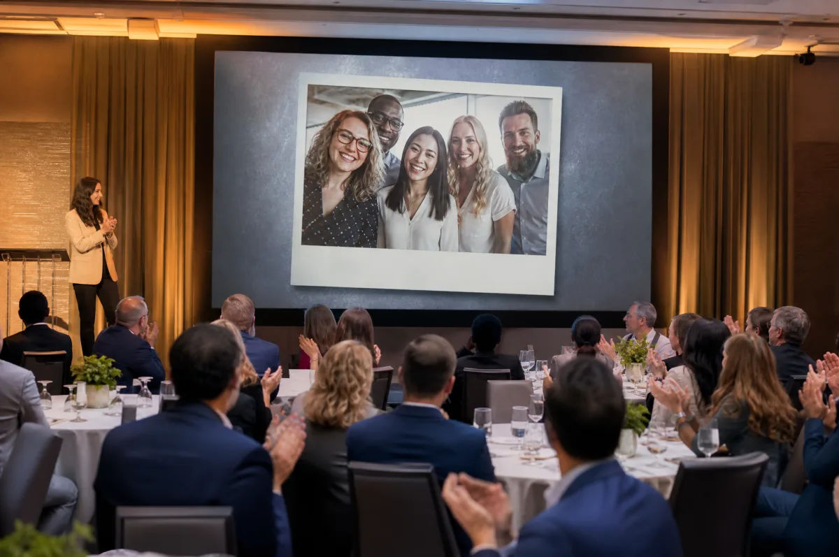 At a conference, the audience applauds while a team photo shows on screen